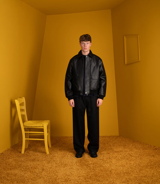 Model wearing the black Carhartt WIP Arizona Jacket with black trousers in a yellow room